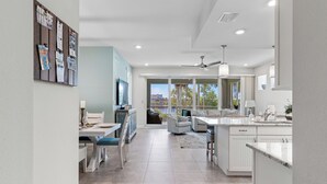 A modern kitchen with white cabinets, a dining area with a table and chairs, and a view through glass doors to an outdoor patio. - Otter Lagoon at One Particular Harbour  379-103 Lagoon Views · Gaming · 3BR (Bradenton)