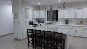 A modern kitchen with white cabinets, a large island with a bar stool, and pendant lighting. - Linda Vista (Tronadora)