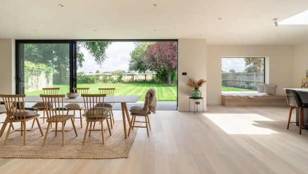 Une pièce spacieuse dotée d’une grande porte-fenêtre coulissante donnant sur un jardin. On y trouve un coin repas avec des chaises et une table en bois, ainsi qu’un coin salon avec un canapé et une table basse.
