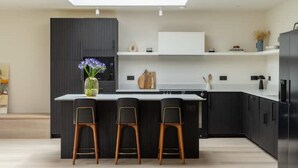 Une cuisine moderne dotée d’un îlot central, de tabourets de bar, de meubles de rangement aux couleurs sombres et d’un four encastré.