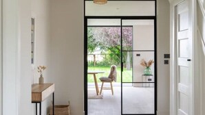 Un couloir moderne avec un plancher en bois, une porte coulissante à cadre noir et un luminaire suspendu.