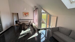 A spacious living area with a large window, a sofa, a dining table with chairs, and a radiator. - Apartment in Laatzen! contactless check-in 11P (Laatzen)