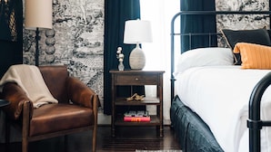 A bedroom with a bed, a nightstand with a lamp, a chair, and a bookshelf.