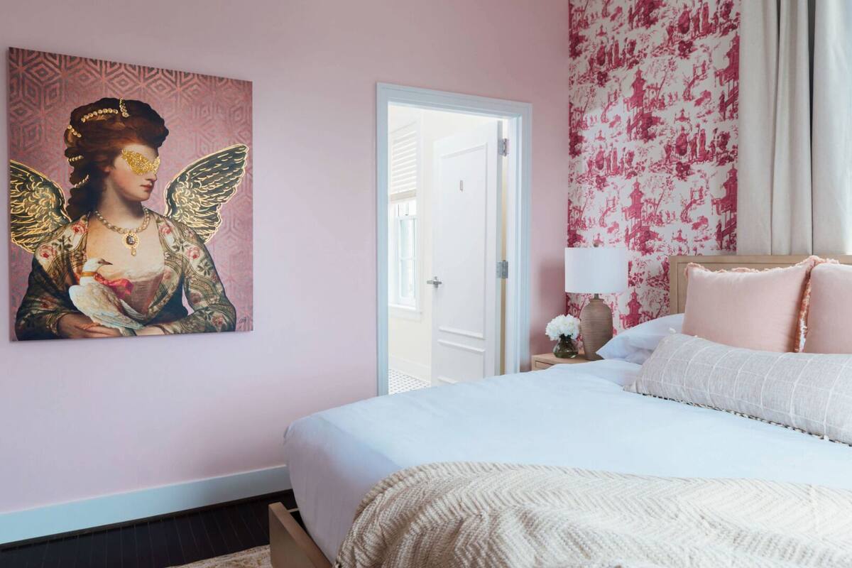 A bedroom with a large bed, a door, a wall with a floral pattern, and a painting of a woman with wings.