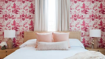 A bedroom with a bed, two nightstands, a window with curtains, and floral wallpaper.