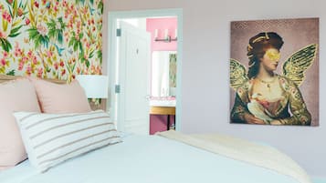 A bedroom with a bed, pillows, a wall with a floral pattern, and a painting of a figure with wings.