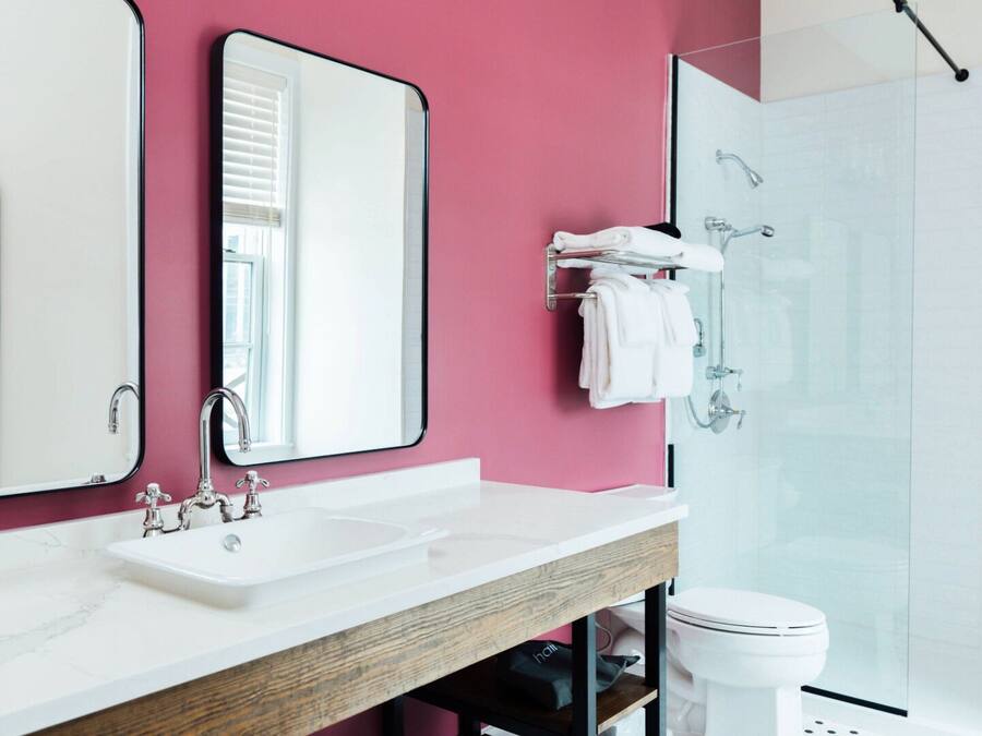 Un baño moderno con una pared rosa, un espejo grande, un lavabo blanco y una cabina de ducha de cristal.
