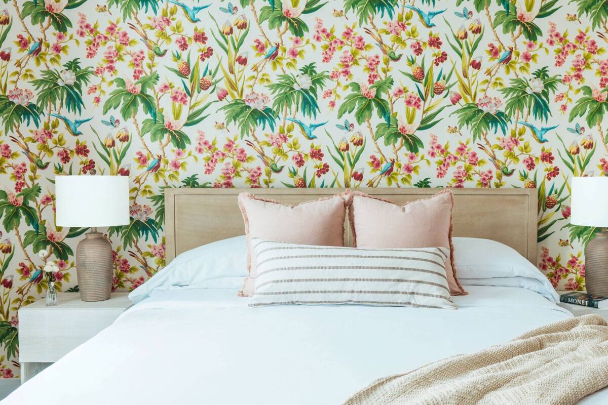 A bedroom with a floral wallpaper, a bed with white bedding, two nightstands with lamps, and a bedside table with a book.