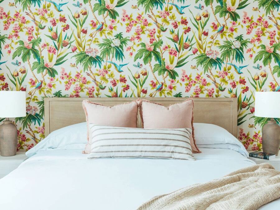 A bedroom with a floral wallpaper, a bed with white bedding, two nightstands with lamps, and a bedside table with a book.
