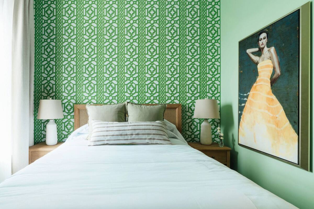 A neatly made bed with white linens, two bedside lamps, and a green patterned wallpaper.