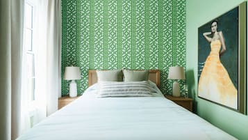 A neatly made bed with white linens, two bedside lamps, and a green patterned wallpaper.