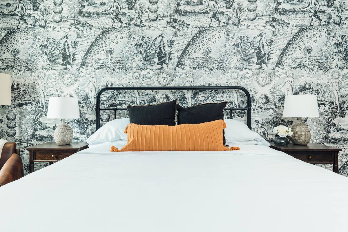 A bedroom with a bed, two nightstands, and a patterned wallpaper.