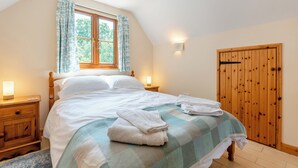Een slaapkamer met een bed, nachtkastjes, een raam met gordijnen, een houten garderobe en een geruit sprei.
