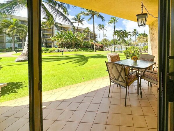 A patio with a table and chairs, a yellow awning, and a view of a well-maintained lawn and palm trees.