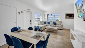 Una sala de estar moderna con un sofá, una mesa de comedor con sillas, una zona de cocina y un ventanal con vistas.