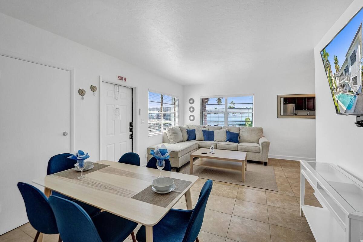 Un salon moderne comprenant un canapé, une table à manger avec des chaises, un coin cuisine et une grande fenêtre donnant sur un beau paysage.