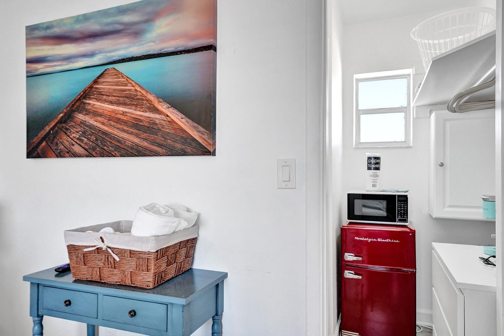 A bathroom with a wooden dock painting, a blue vanity, a red vintage refrigerator, and a microwave.
