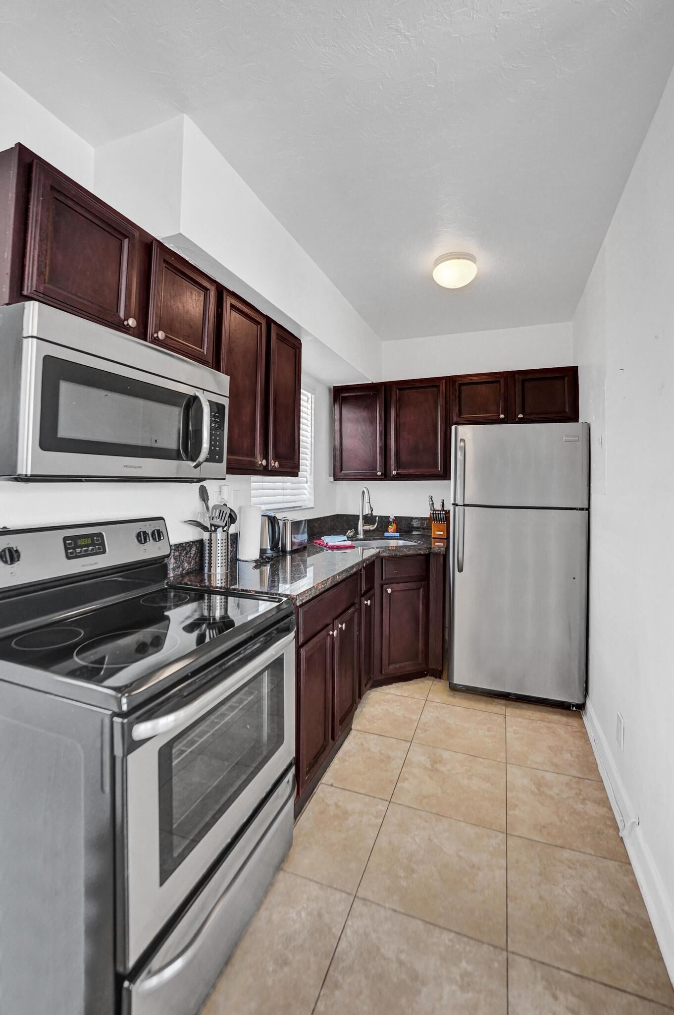 A kitchen with dark wooden cabinets, stainless steel appliances, and a tiled floor.