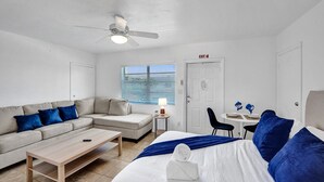 Una habitación moderna y bien iluminada con sofá, cama, una mesita y un ventilador de techo.