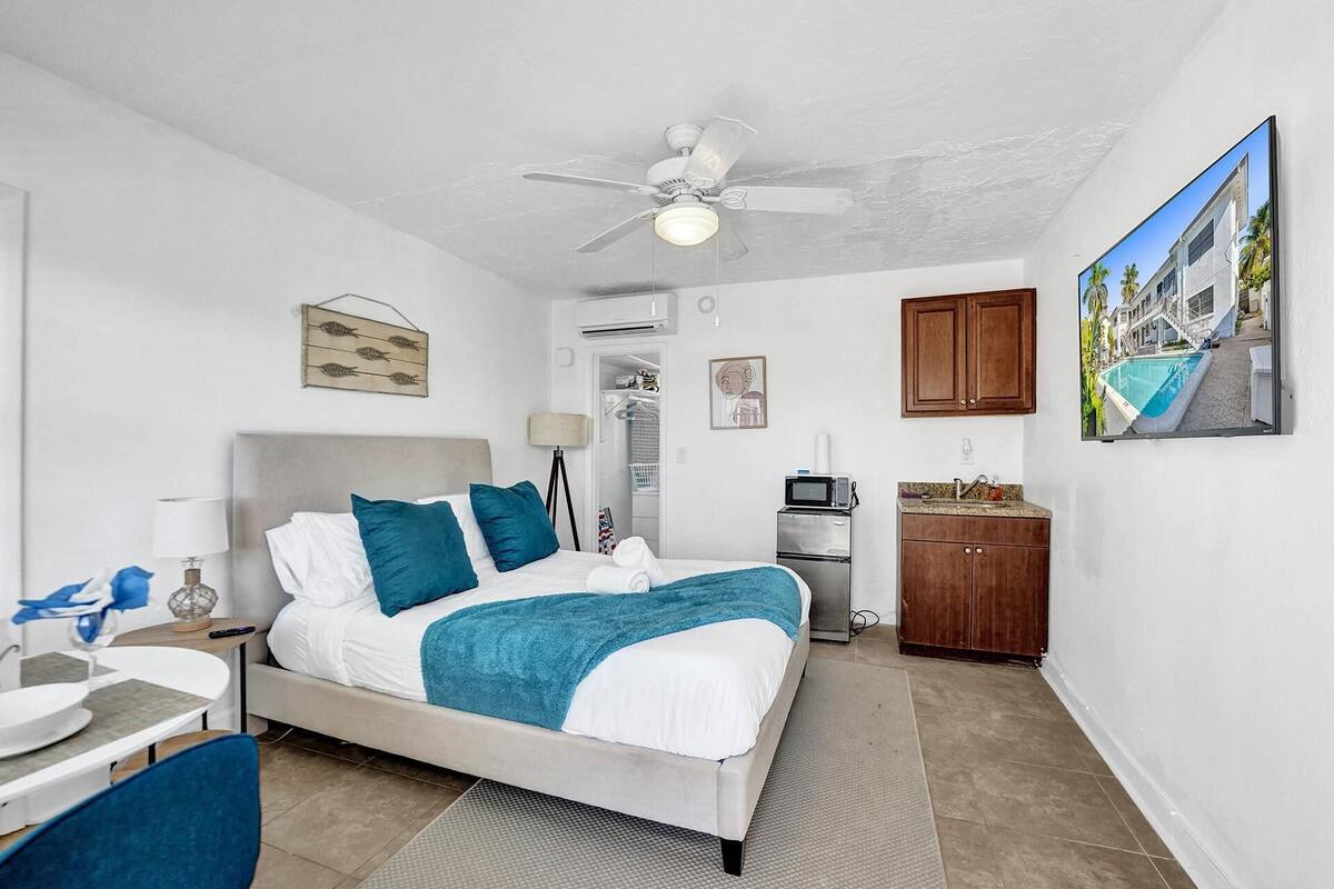 Une chambre à coucher comprenant un lit, un bureau, une chaise, un ventilateur de plafond, un four à micro-ondes, une armoire et un tableau accroché au mur.