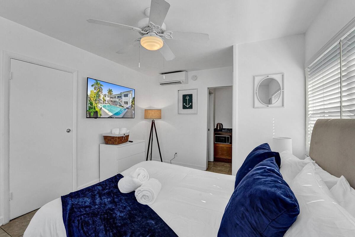 Une chambre d’hôtel avec un lit, un ventilateur de plafond, une télévision, une lampe et une vue sur l’extérieur.
