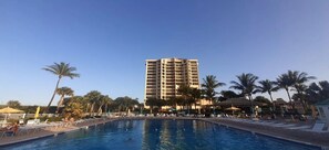 A hotel with a swimming pool, palm trees, and a tall building in the background.