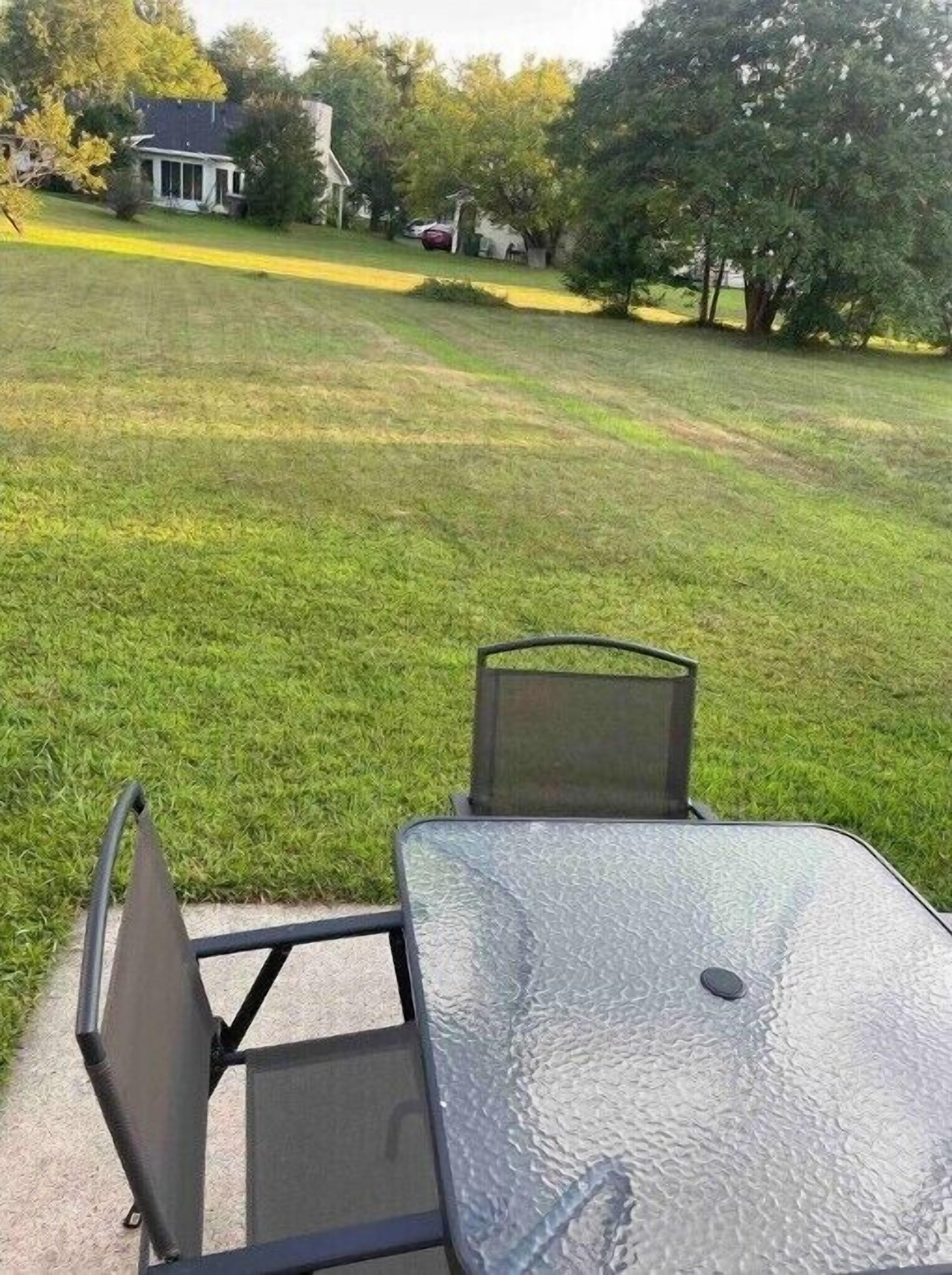 Un'area patio con tavolo e sedie, un prato e una casa sullo sfondo.