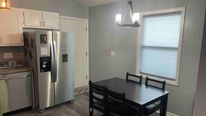 A compact kitchen with white cabinets, a stainless steel refrigerator, a coffee maker, and a dining table with chairs. - Remodeled duplex near coliseum (Greensboro)
