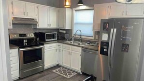 A modern kitchen with white cabinets, stainless steel appliances, and a black countertop. - Remodeled duplex near coliseum (Greensboro)