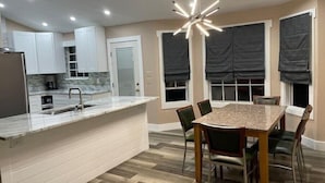A modern kitchen with white cabinets, a marble countertop, and a built-in island with a sink. - Experience Tallahassee near FSU - Just a 12-min Drive (Tallahassee)