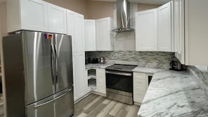 A modern kitchen with white cabinets, stainless steel appliances, and a marble countertop. - Experience Tallahassee near FSU - Just a 12-min Drive (Tallahassee)