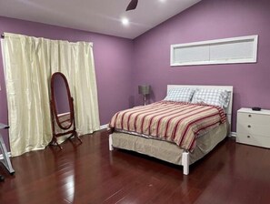 Cozy retreat with a single bed, nightstand, and dresser, featuring a window with blinds and a ceiling fan.