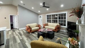 A modern living room with two sofas, a coffee table, and a yellow armchair. There is a TV and a fireplace with a vase of flowers. - Experience Tallahassee near FSU - Just a 12-min Drive (Tallahassee)