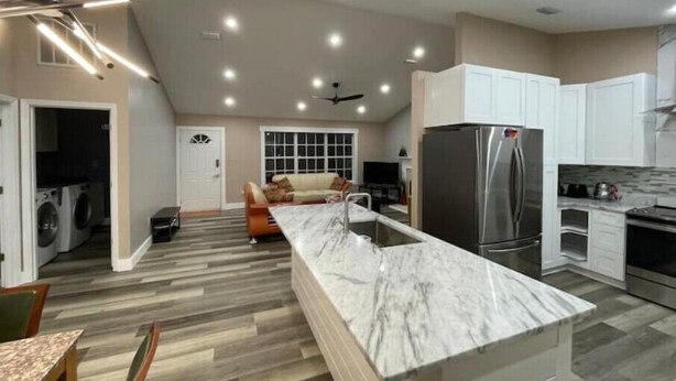 A modern kitchen with a marble island, stainless steel appliances, and a dining area with a wooden table and chairs. - Experience Tallahassee near FSU - Just a 12-min Drive (Tallahassee)