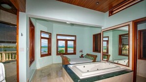 A bathroom with a large bathtub, a shower area, and a view of the ocean through large windows.