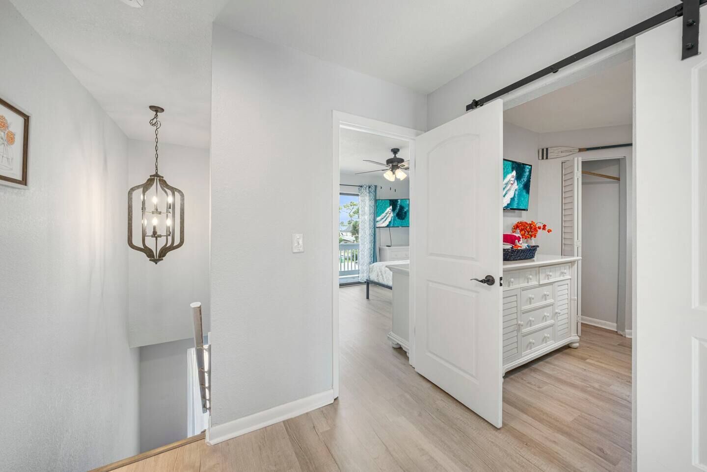 A hallway with a white door leading to a bedroom, a white dresser with drawers, and a ceiling fan.