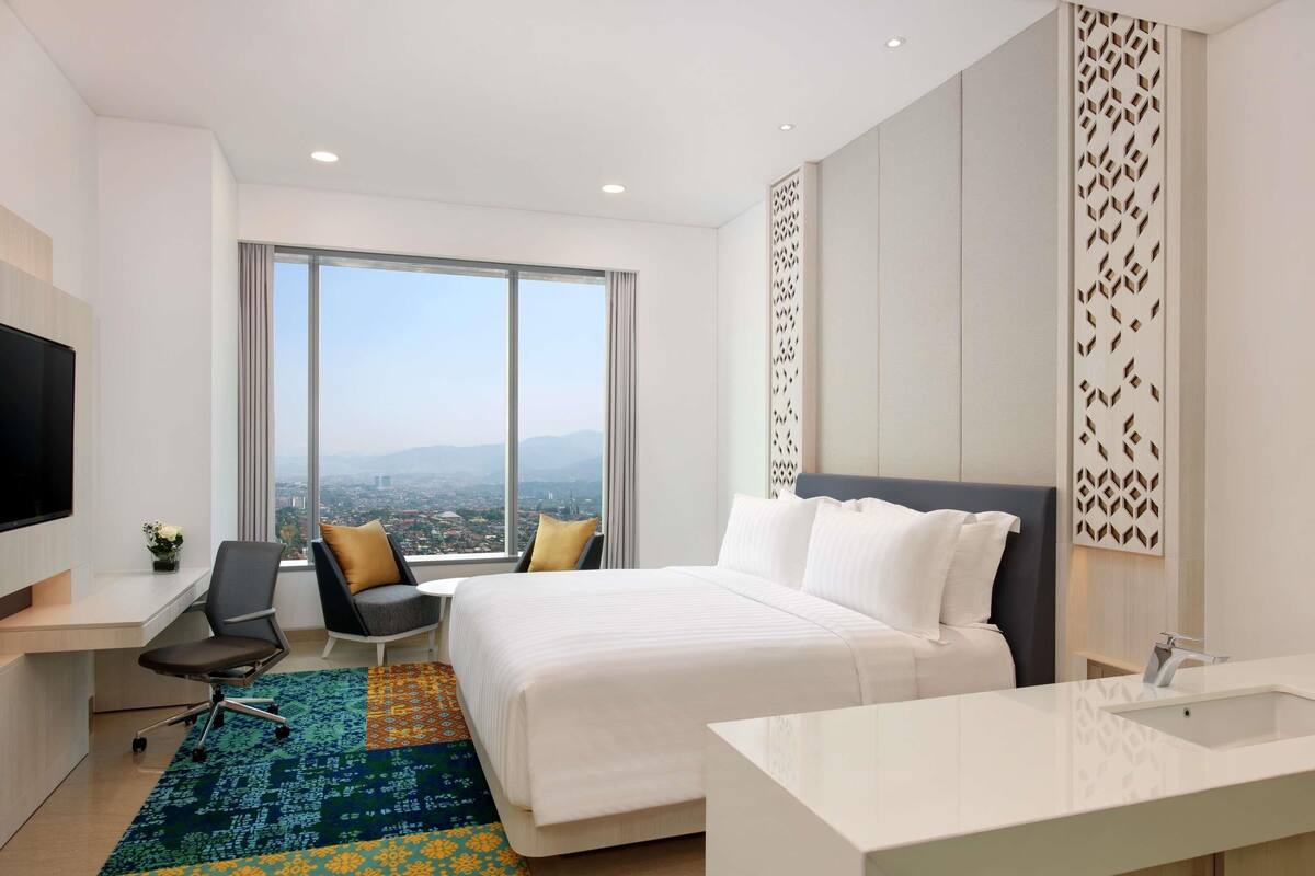 A modern hotel room with a large bed, a desk, a chair, and a TV.