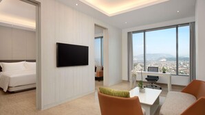 Ett modernt hotellrum med en säng, ett skrivbord, en stol, en TV och ett stort fönster med utsikt över staden.