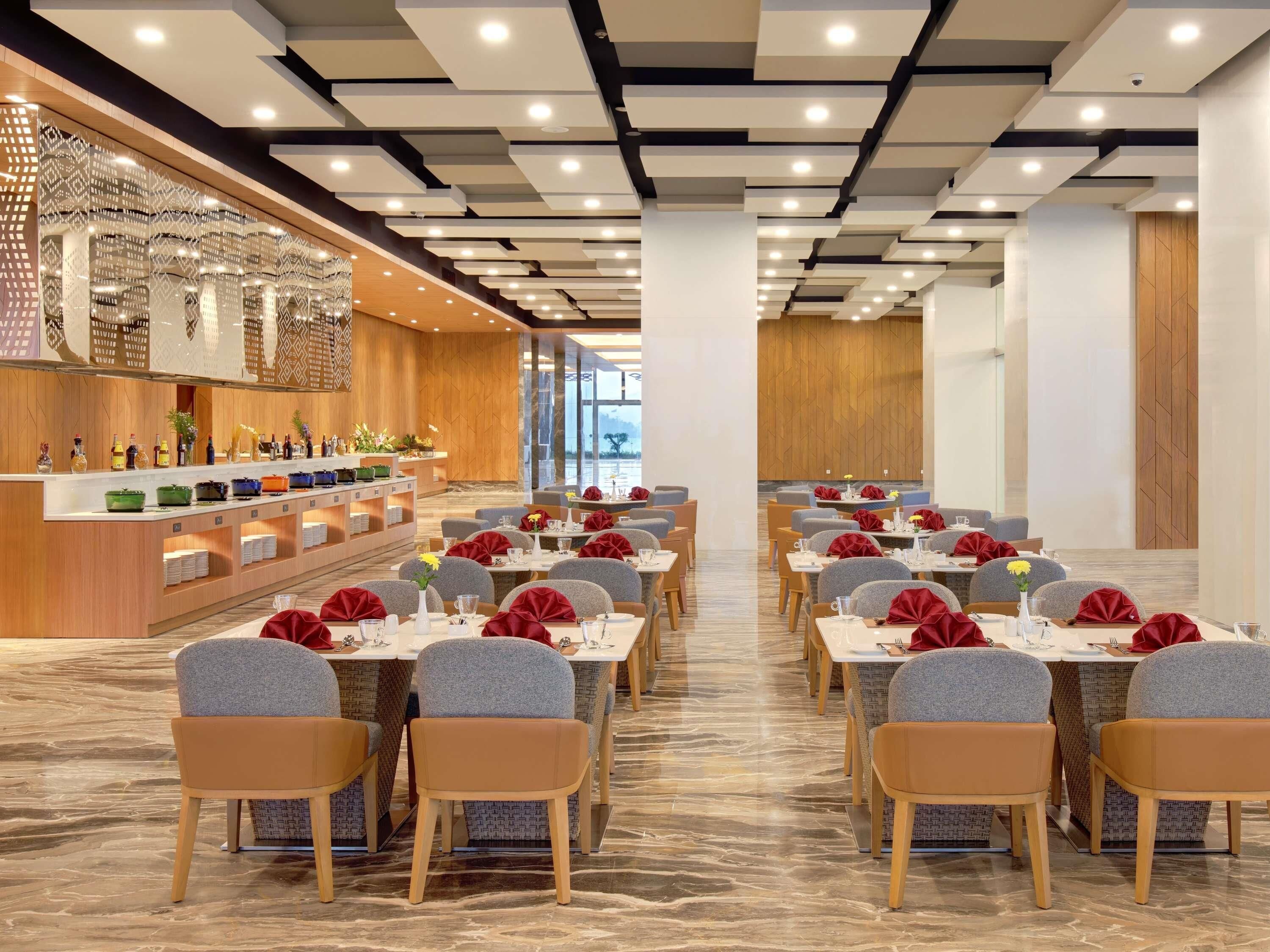 A modern dining area with marble flooring, grey upholstered chairs, and tables set with red napkins and glassware.