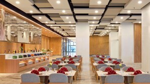 A modern dining area with marble flooring, grey upholstered chairs, and tables set with red napkins and glassware. - Grand Mercure Lampung (Bandar Lampung)