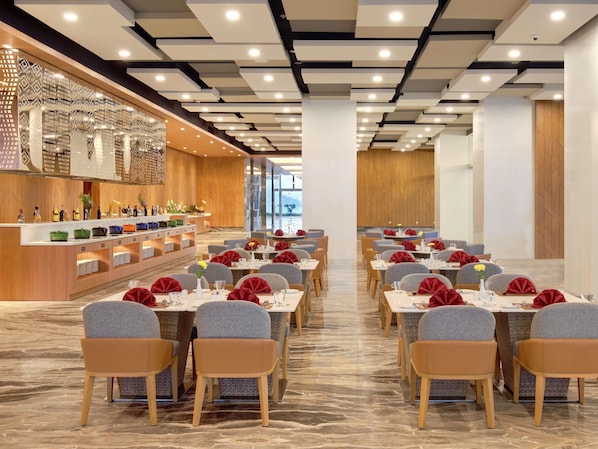 A modern dining area with marble flooring, grey upholstered chairs, and tables set with red napkins and glassware.