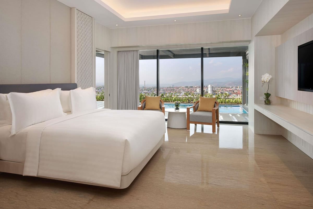 A modern hotel room with a large bed, a TV mounted on the wall, and a balcony with a pool view.