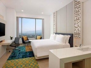 A modern hotel room with a large bed, a desk, a chair, and a TV.