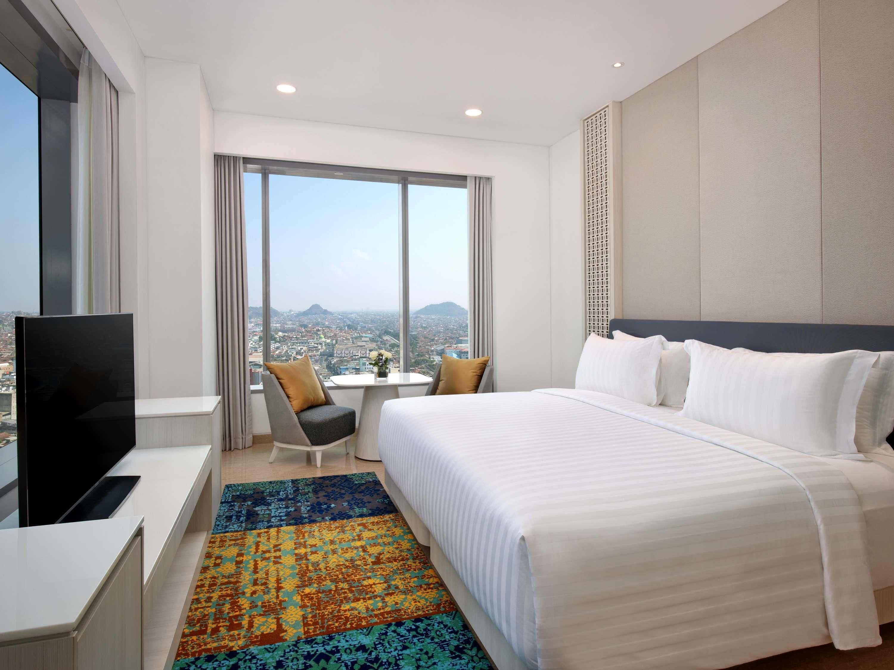 Habitación de hotel con una cama grande, televisión, escritorio y vista a la ciudad.