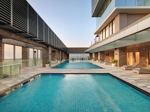 A modern indoor swimming pool with two separate sections, surrounded by a glass railing and a stone wall. - Grand Mercure Lampung (Bandar Lampung)