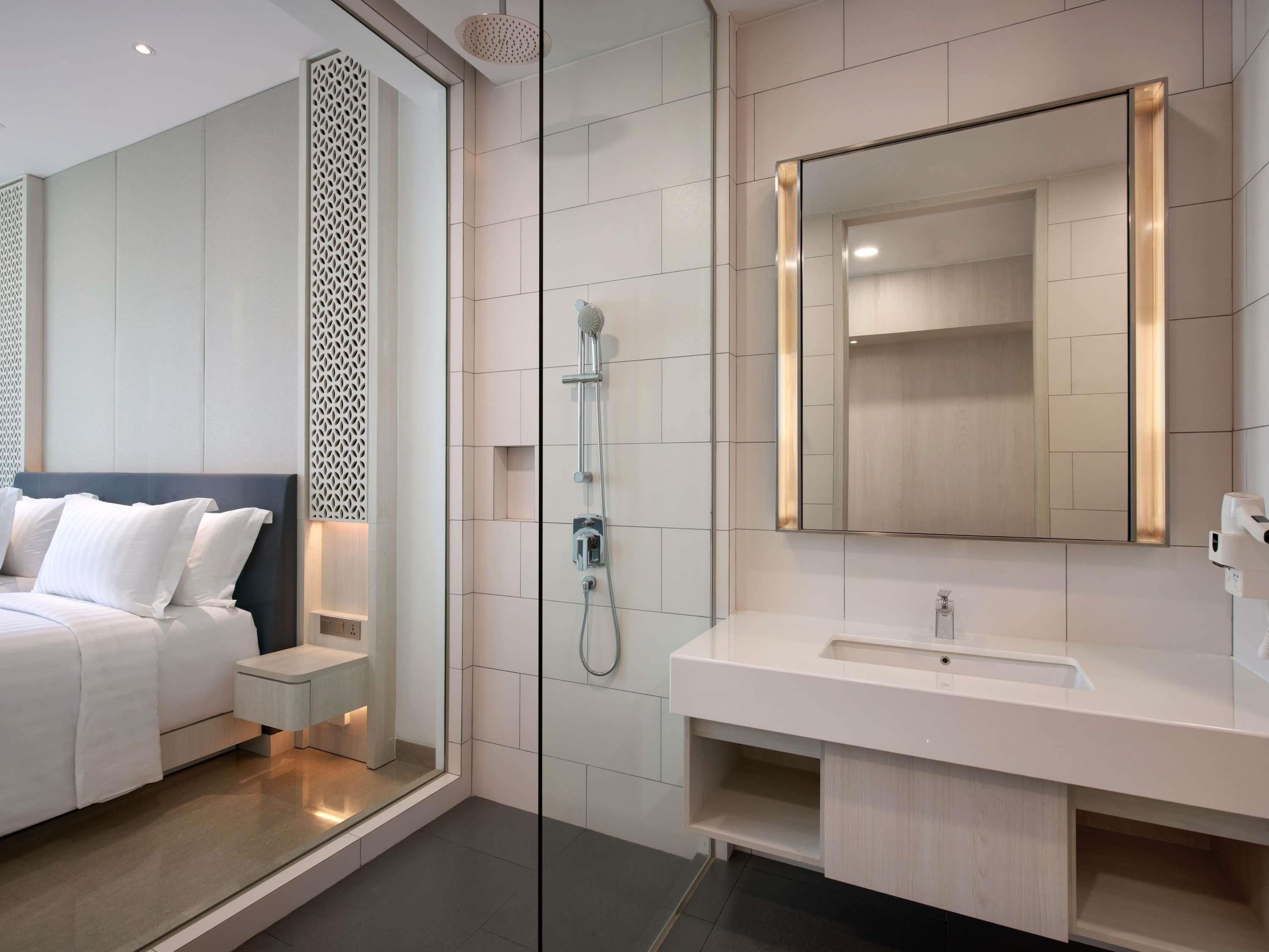 Una habitación de hotel moderna con una cama, ducha, un espejo grande y una tocador con lavabo.