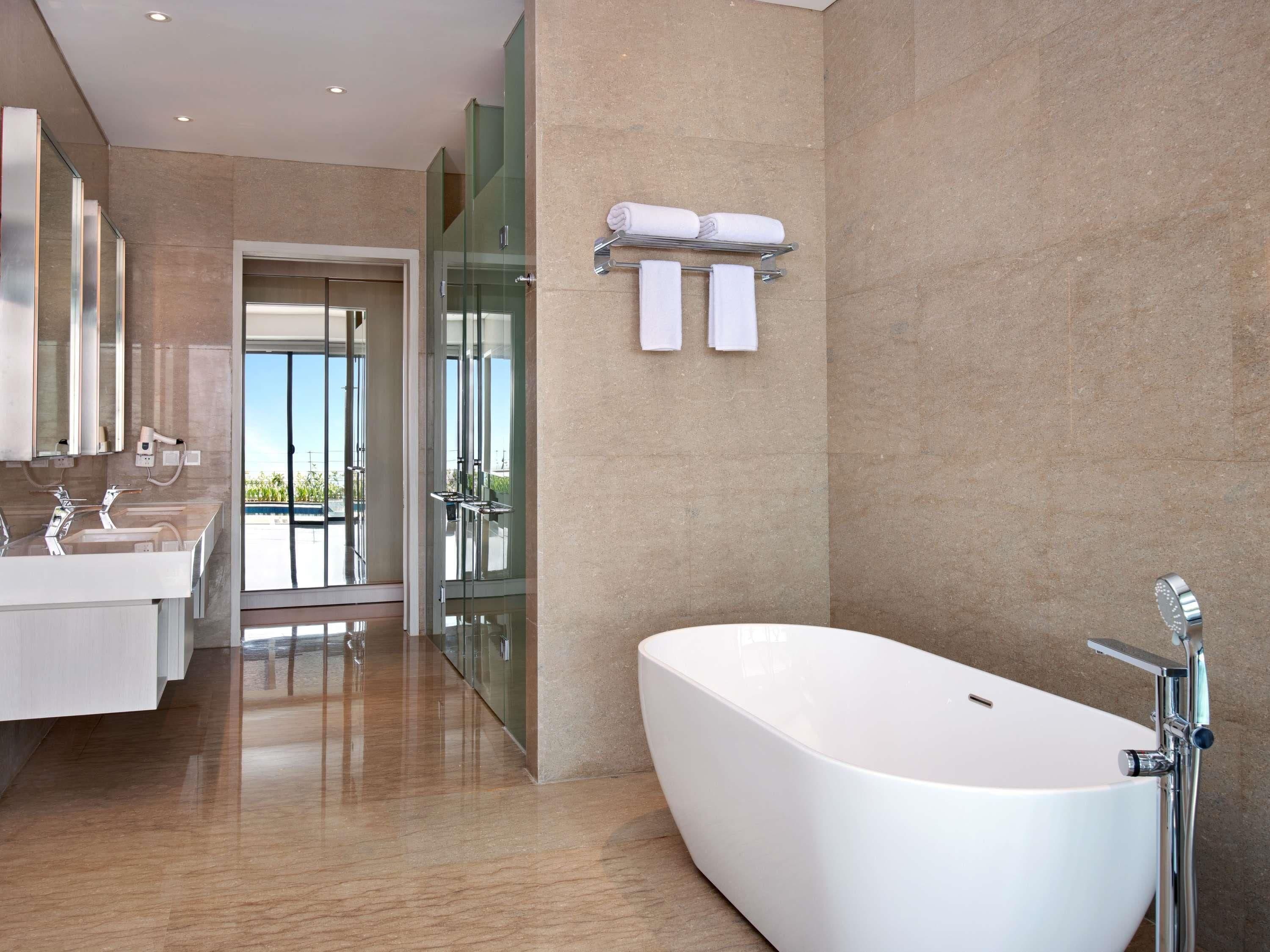 A modern bathroom with a large bathtub, two sinks, a glass shower enclosure, and a view through the glass door.