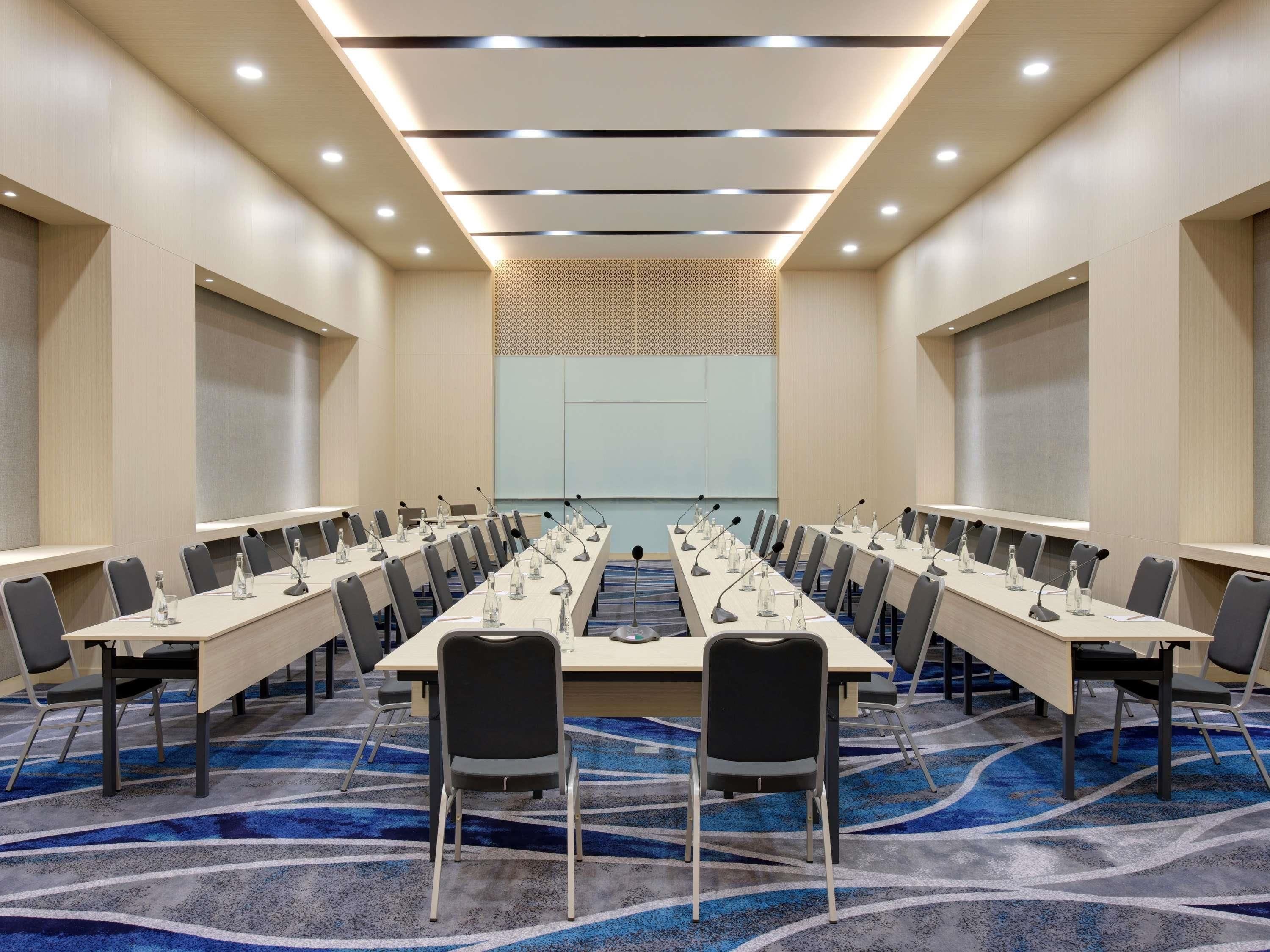 A conference room with a long table, multiple chairs, microphones, and a carpeted floor.