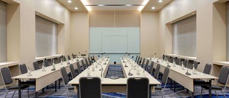 A conference room with a long table, multiple chairs, microphones, and a carpeted floor.