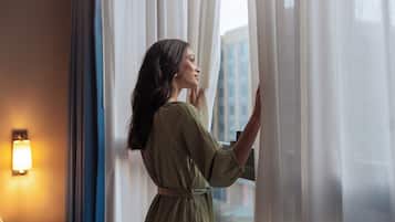 A person adjusting curtains in a room with a lamp on the wall and a small round table.